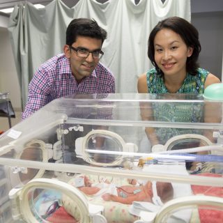 Associate Professor Rebecca Lim and Dr Atul Malhotra stand before a premature baby, cradled in a humidicrib at Monash Health