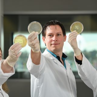 Sam Forster and Gemma D'Adamo and Tam holding up petri dishes conducting research at Hudson Institute