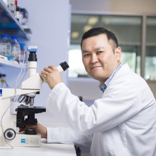 Dr Joohyung Lee, Honorary Research Associate, working at the lab bench and using a microscope to assist with his medical research